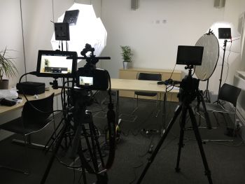 A lot of filming equipment pointing towards a desk and chair with nobody in the frame