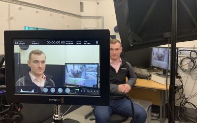An picture from a film set. The subject can be seen sitting down and also on a nearby monitor