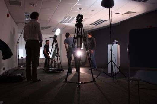 A low shot of a video crew filming a subject matter expert in an office cameras, lights backdrop and props