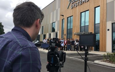 A cameraperson filming a large crowd outside a building with Oxford Space System's logo on