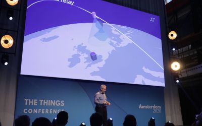 A man presenting on stage with an animation on the screen behind him